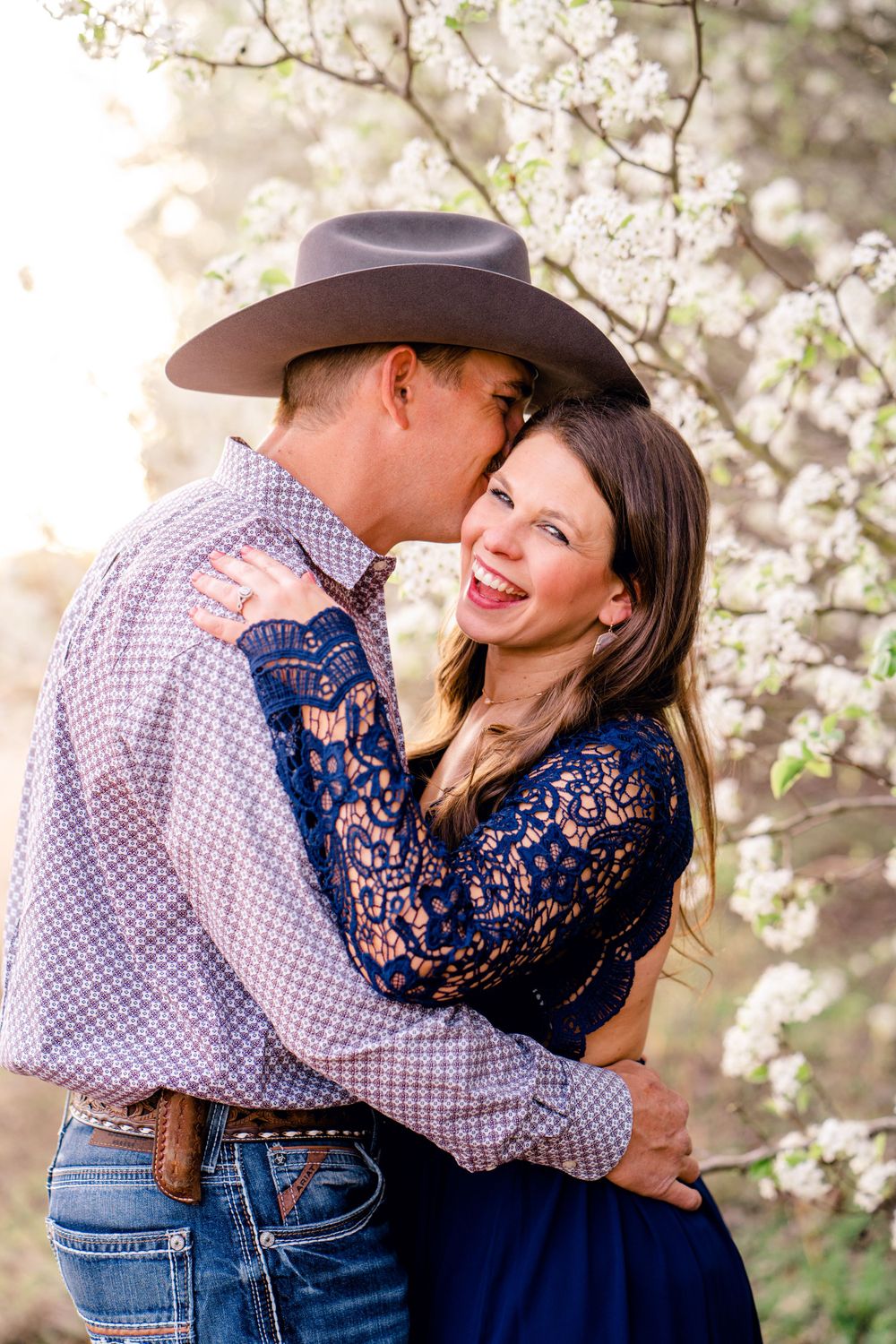Couple in western attire sharing a joyful moment among spring cherry blossoms.