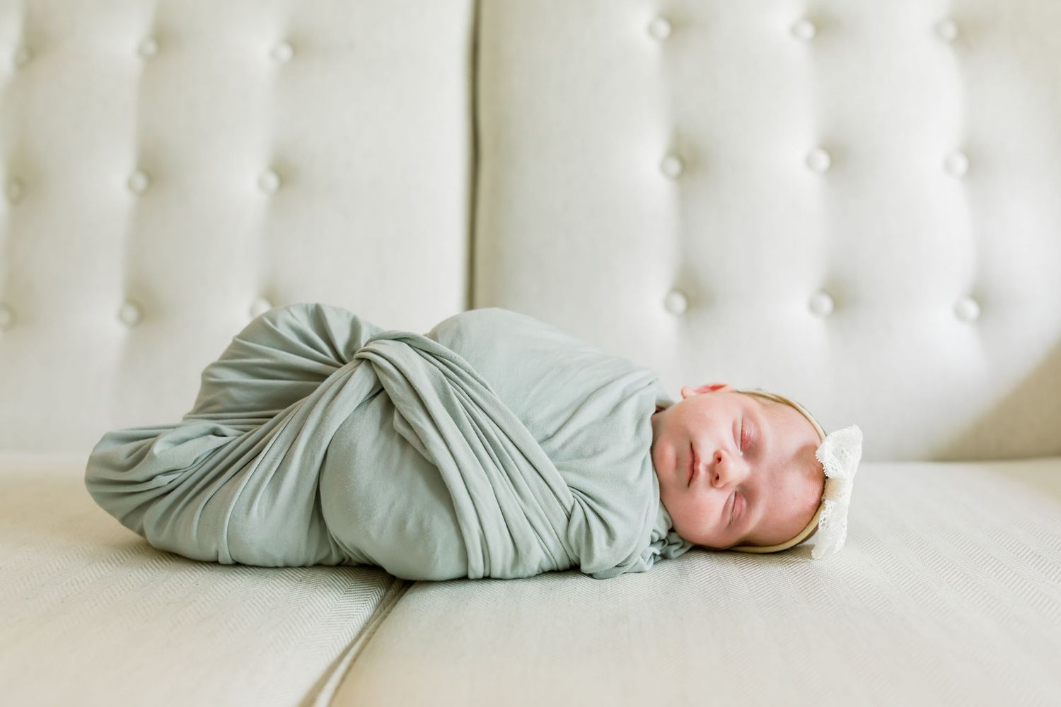 Peaceful newborn baby wrapped in mint green swaddle lying on white cushioned surface.
