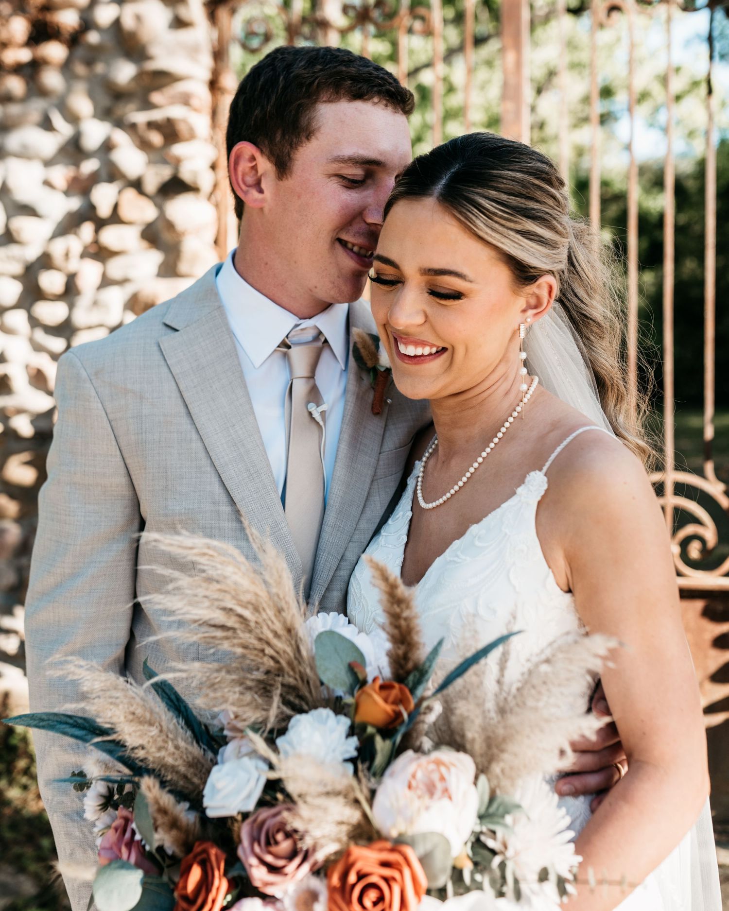 Romantic wedding portrait featuring a light grey suit and white dress with pampas grass bouquet.