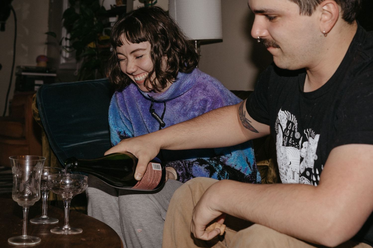Two people relaxing on a couch with wine glasses sharing an intimate moment in dim lighting.