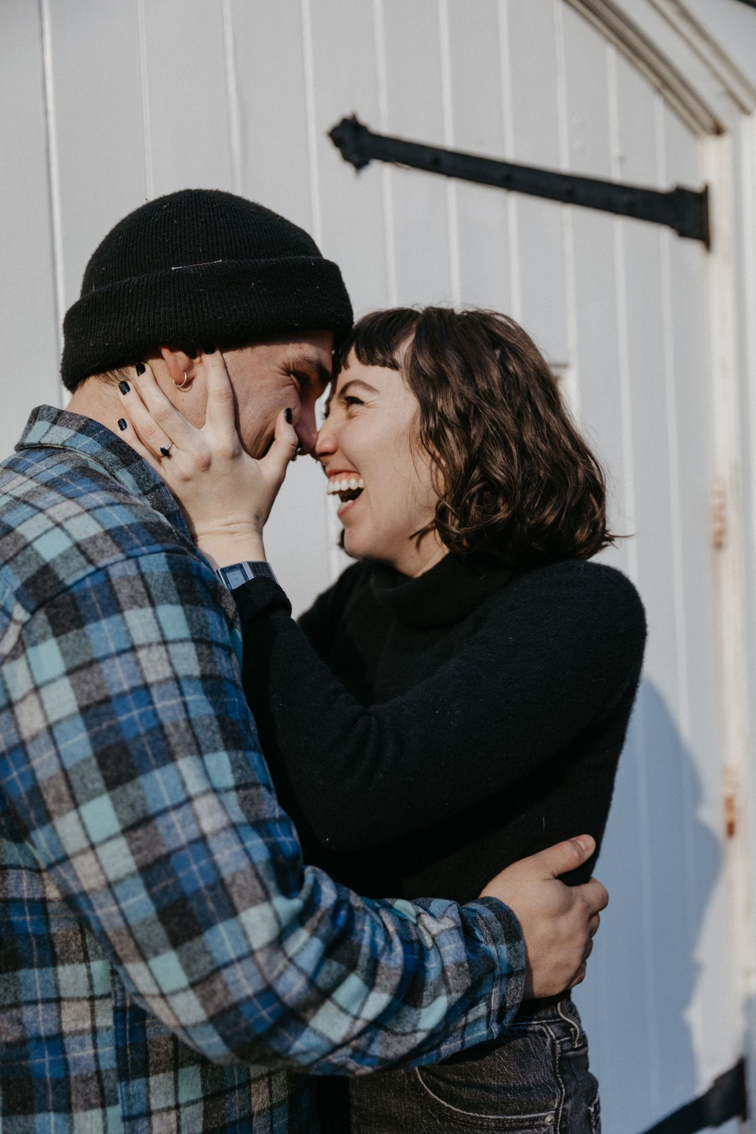 A romantic moment captured between a couple against a white wooden wall.