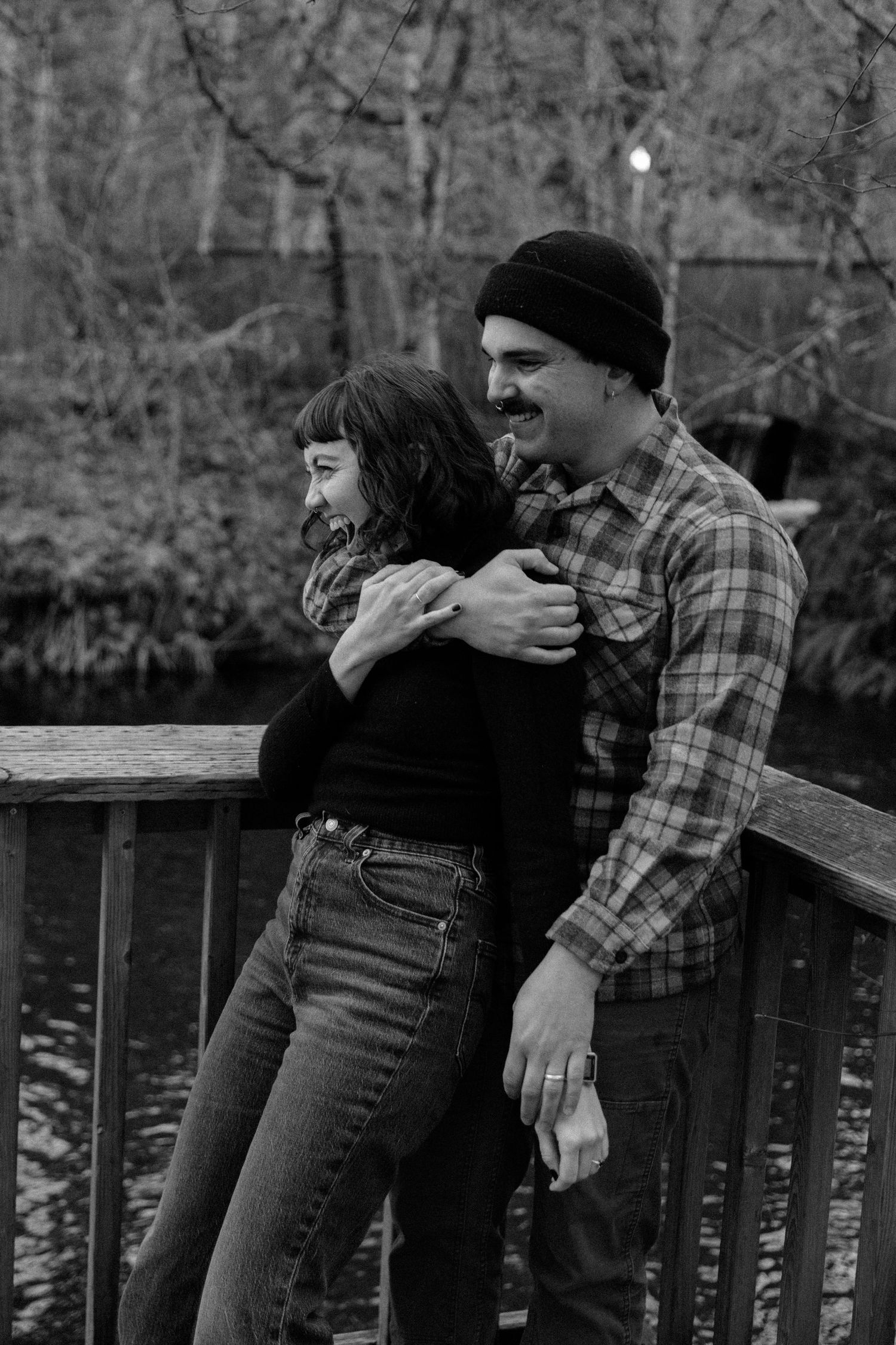 A couple shares a tender moment on a wooden deck with trees in the background.