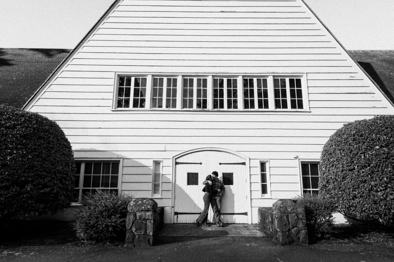 Black and white photo of white A-frame building with central doorway and symmetrical landscaping.