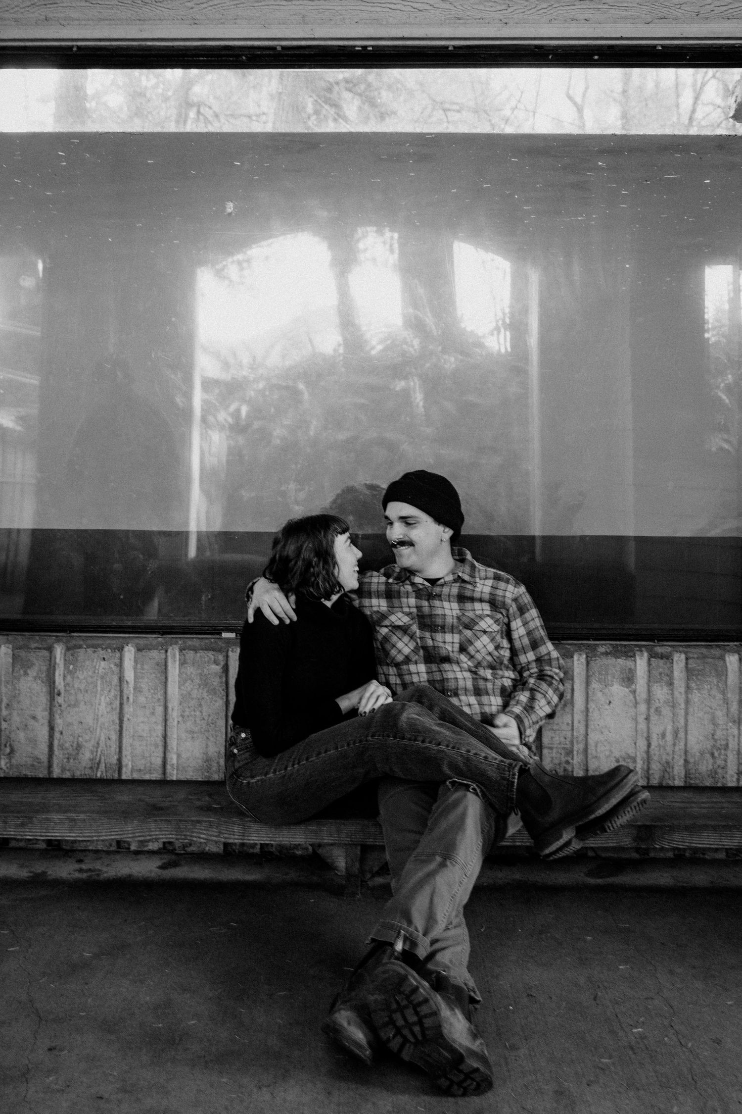 A black and white photo of two people sitting close together on a covered bench.