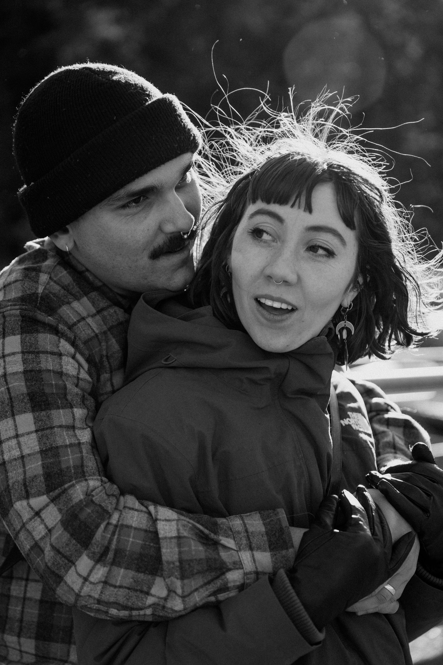 Black and white portrait of a couple sharing an embrace outdoors with backlit hair.