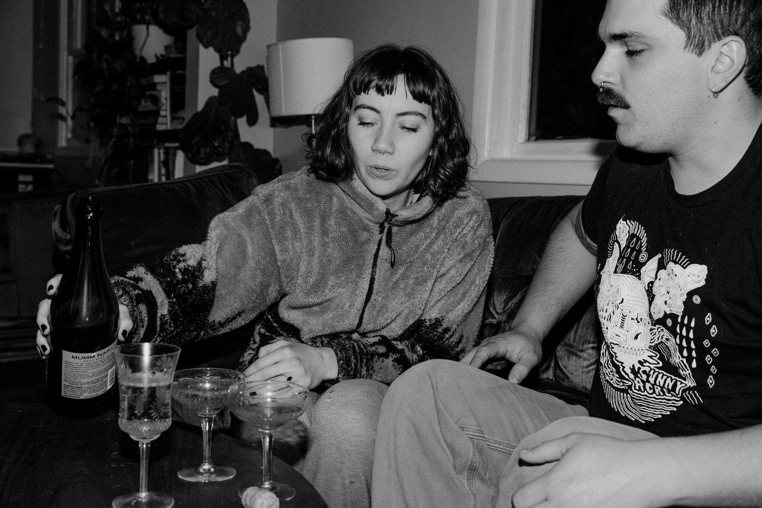A black and white photo of two people sitting together with wine glasses on a couch.