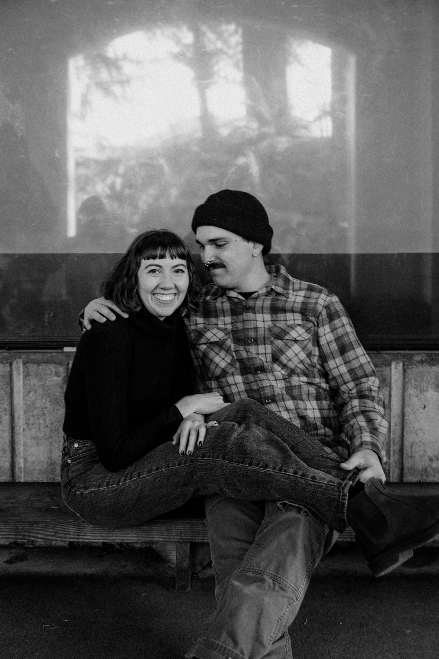 A black and white portrait of a couple sharing an intimate moment on a bench.