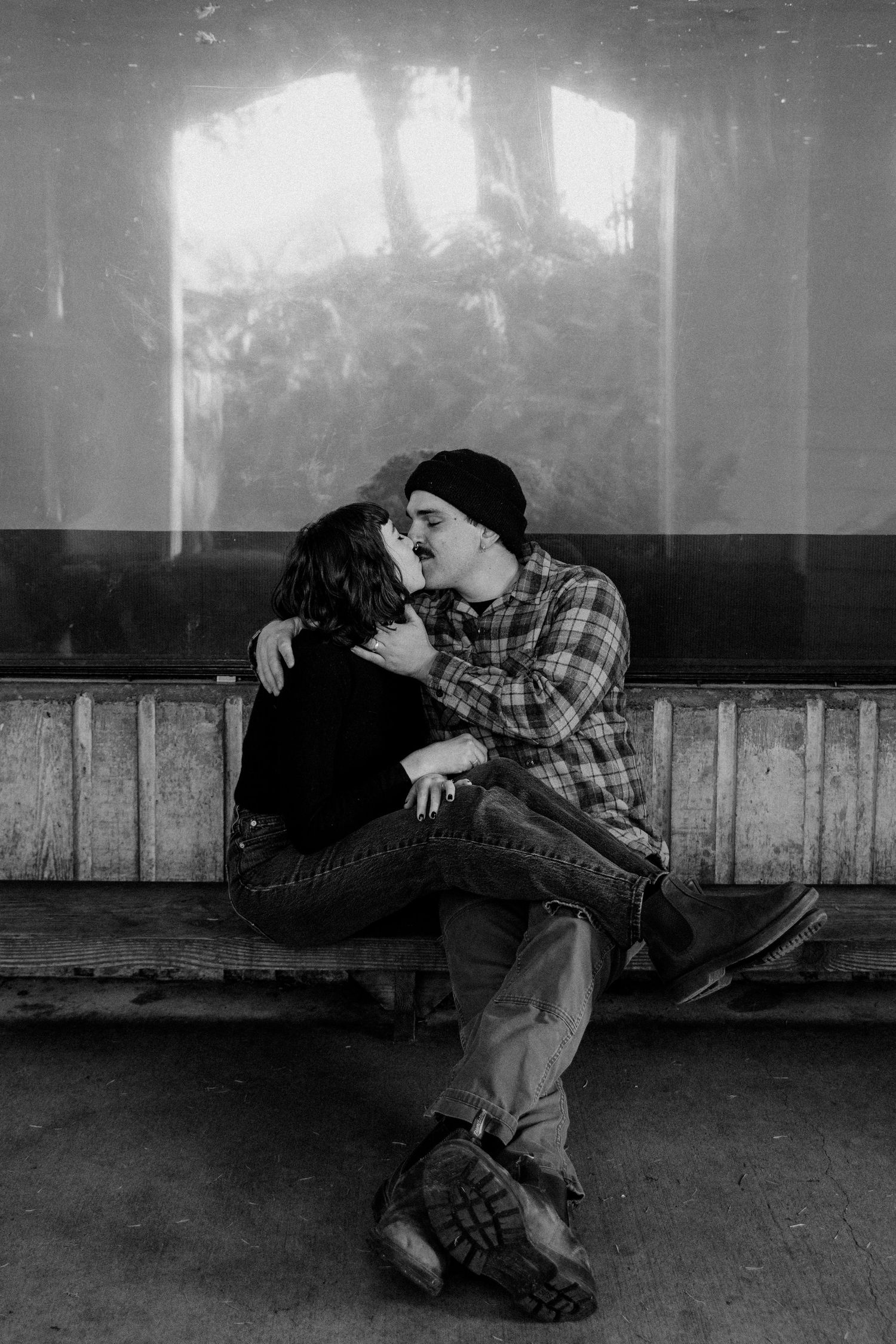 An intimate black and white portrait of two people sharing a tender moment on a bench.