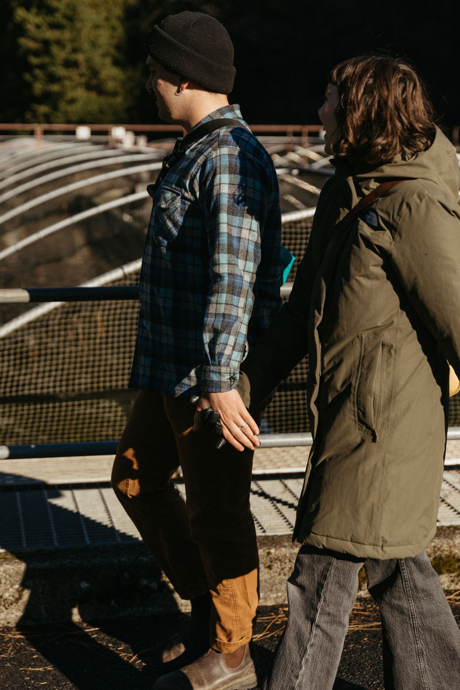 Two people walking together past metal greenhouse structures on a sunny day.