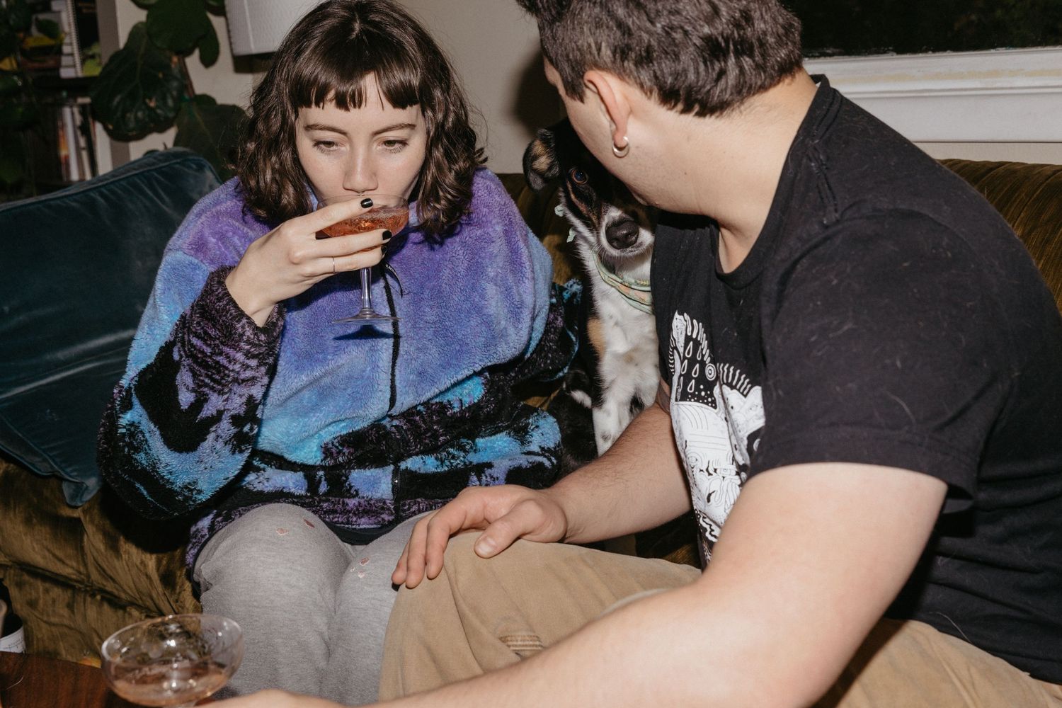 Couple relaxing on couch with wine glasses while petting their cat.
