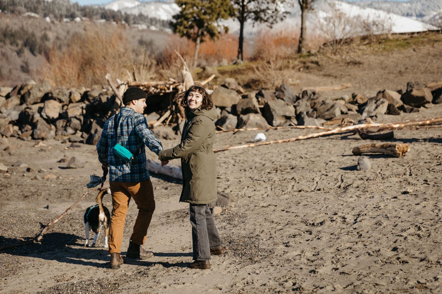 Two people playing with dogs on rocky terrain with mountains in background.