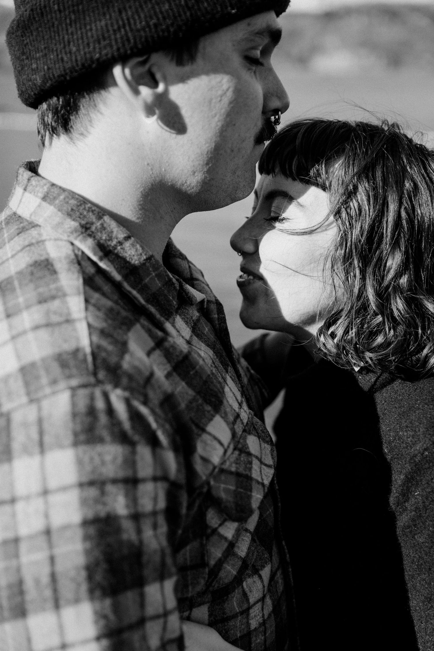 Intimate black and white portrait of a couple in winter wear sharing a close moment outdoors.