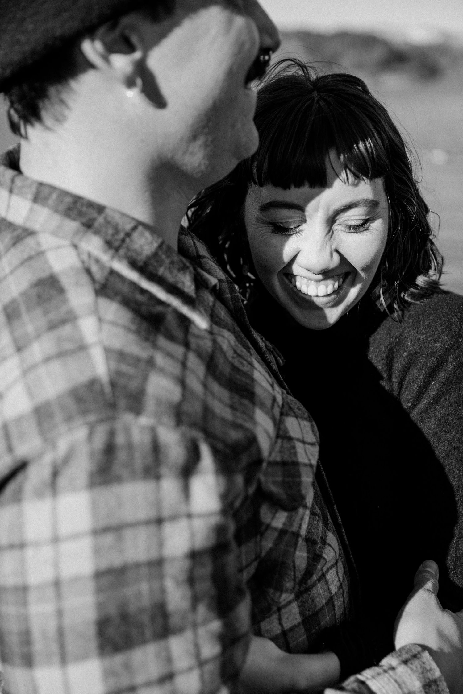 Black and white capture of genuine laughter shared between a couple in outdoor winter clothing.