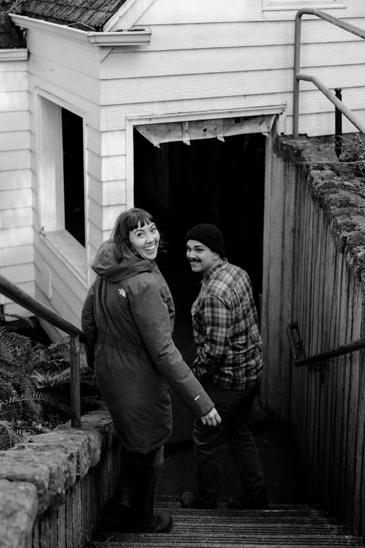 A black and white photo of two people on outdoor stairs leading to a white building entrance.