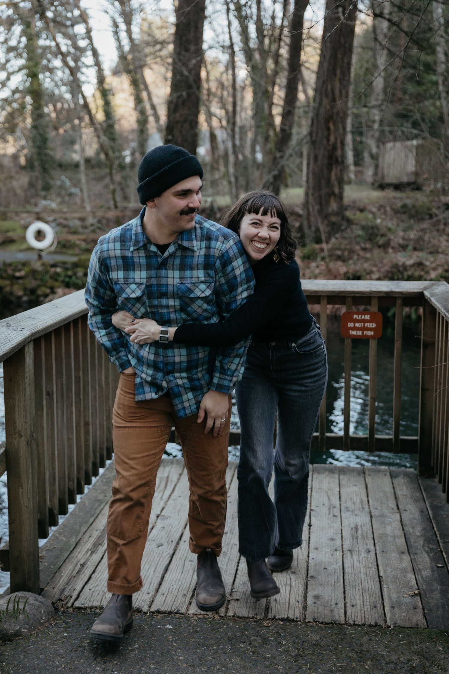 A couple sharing a laugh while standing together on a wooden boardwalk in the woods.