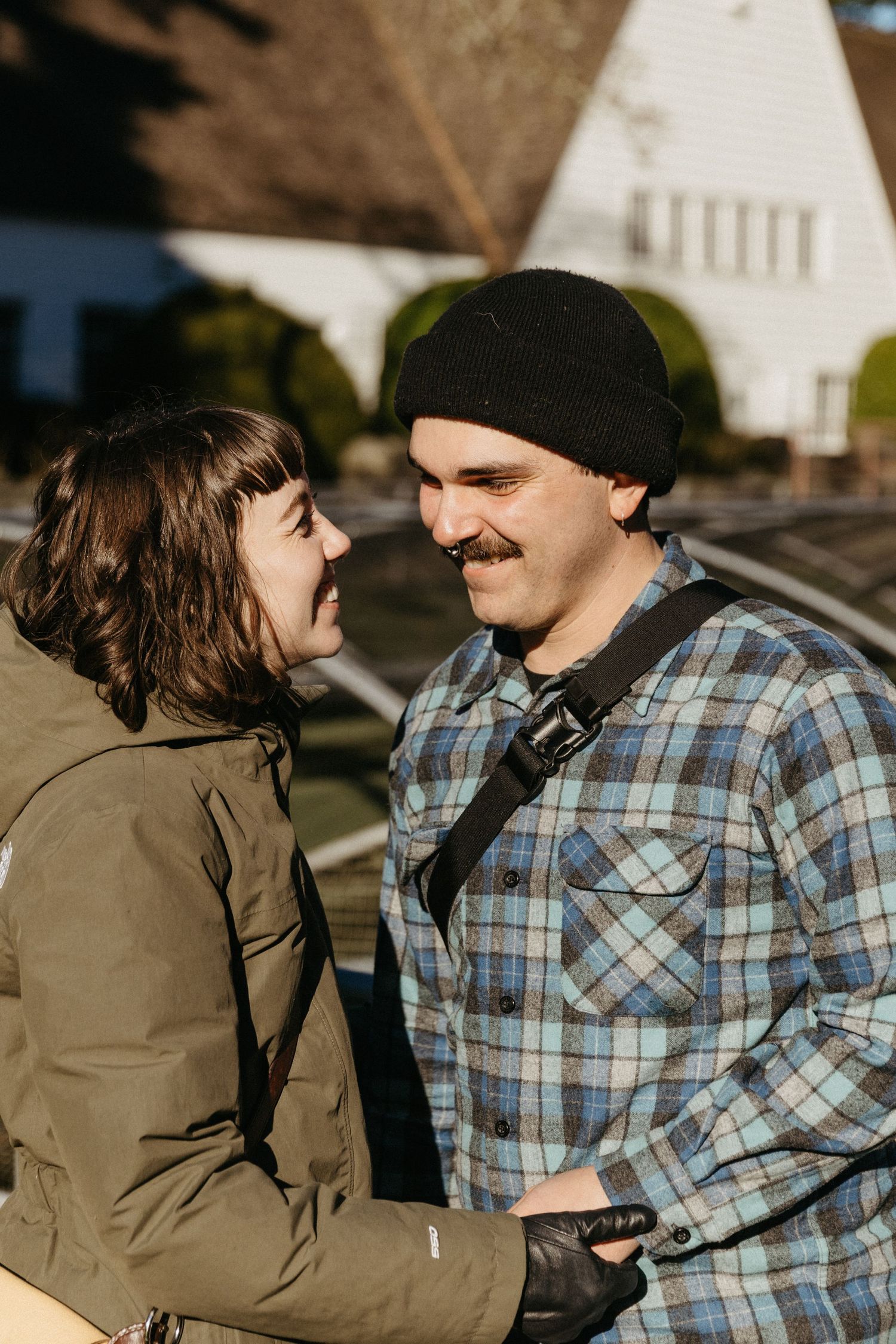 Couple in casual winter wear sharing a laugh outdoors near white buildings.