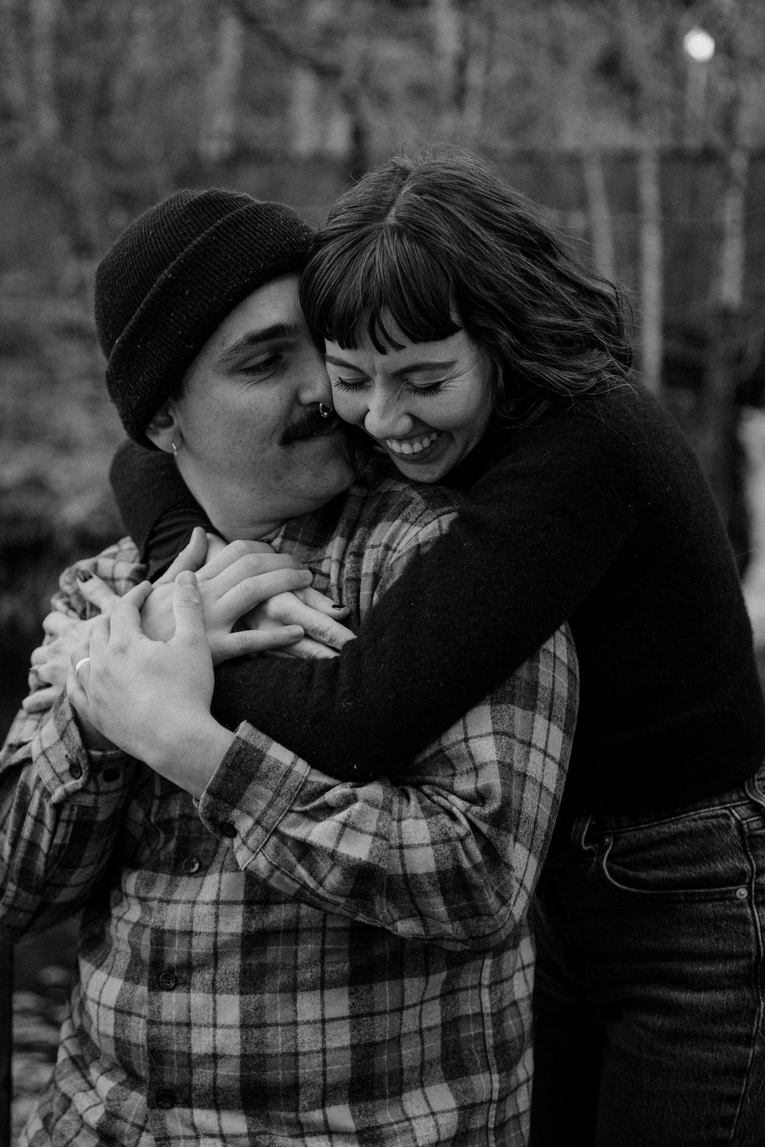A candid black and white photo of a couple embracing and laughing together outdoors.