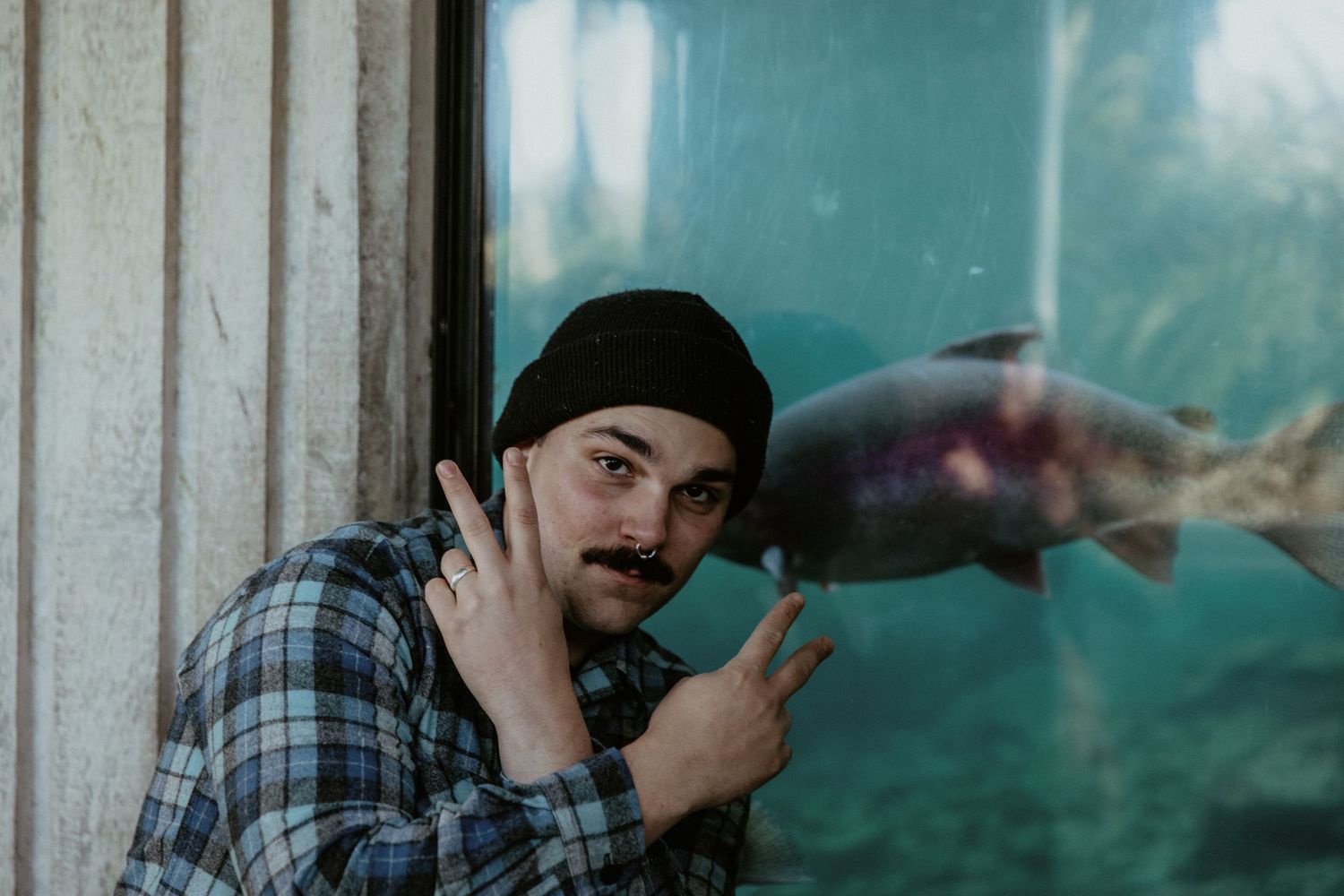A person in plaid points excitedly at a fish swimming behind aquarium glass.
