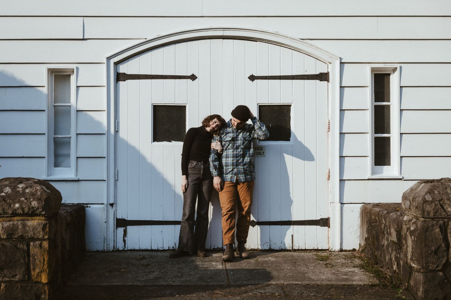 A romantic couple stands together against a rustic white barn door.