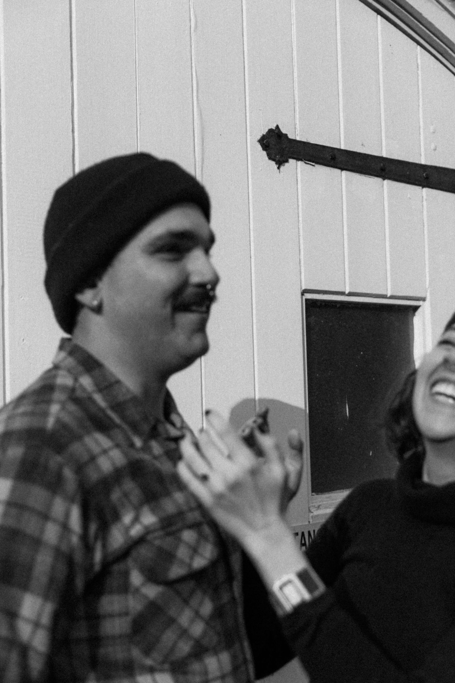 A candid black and white photo of a laughing couple against a white wall.