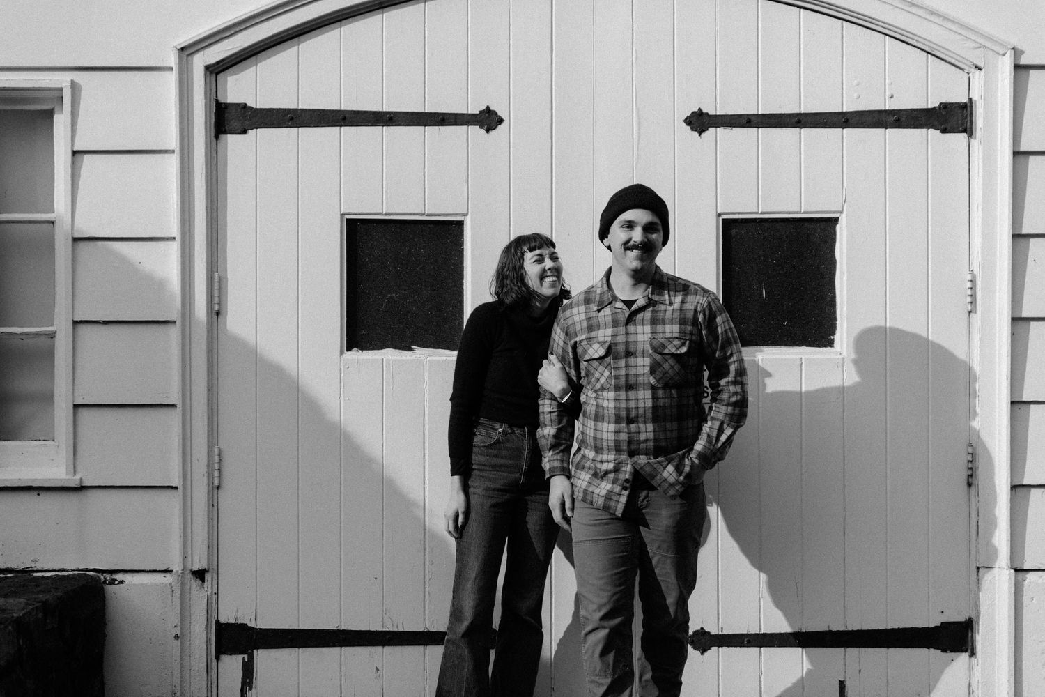 A couple poses casually in front of a white barn door with black hardware.