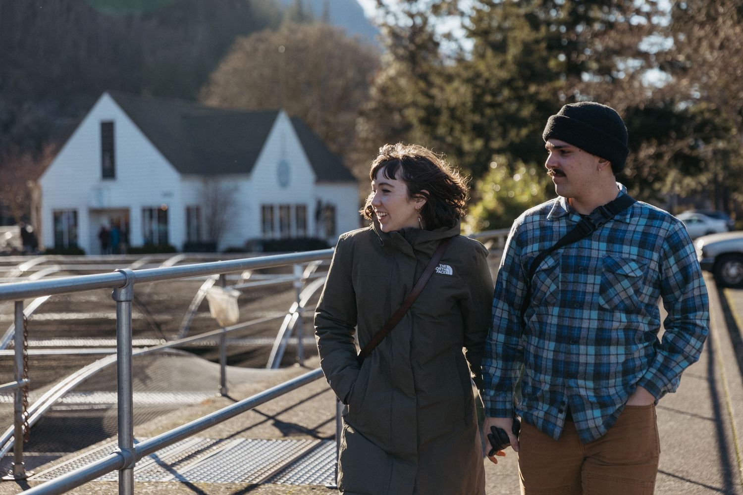 Couple in casual winter wear standing by a white fence on a rural property.
