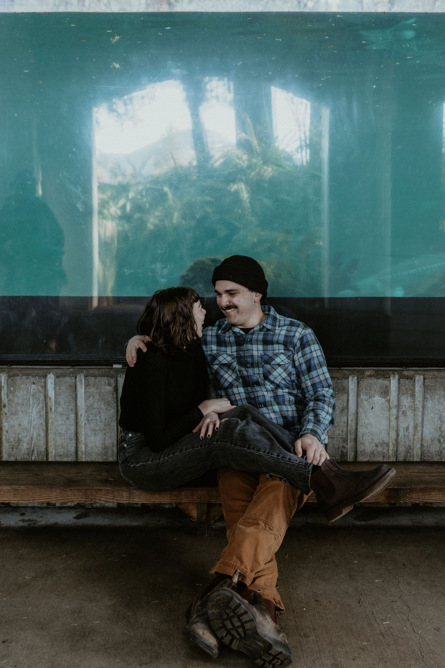 A romantic couple sits together on a bench in front of a teal-tinted window.