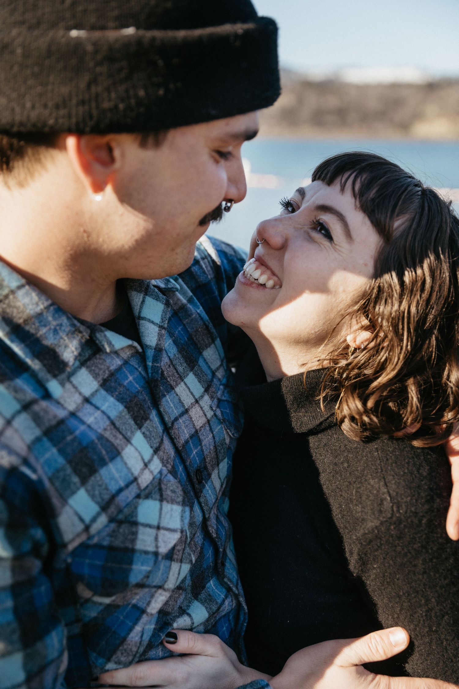 A tender moment shared between a couple against a waterfront background.