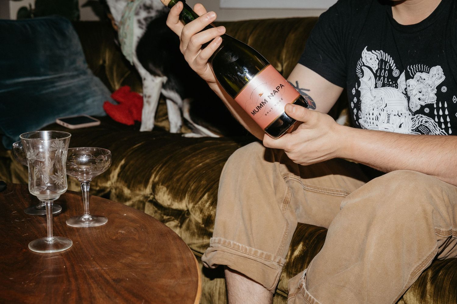 Close-up of hands opening wine bottle with vintage glasses on wooden table.