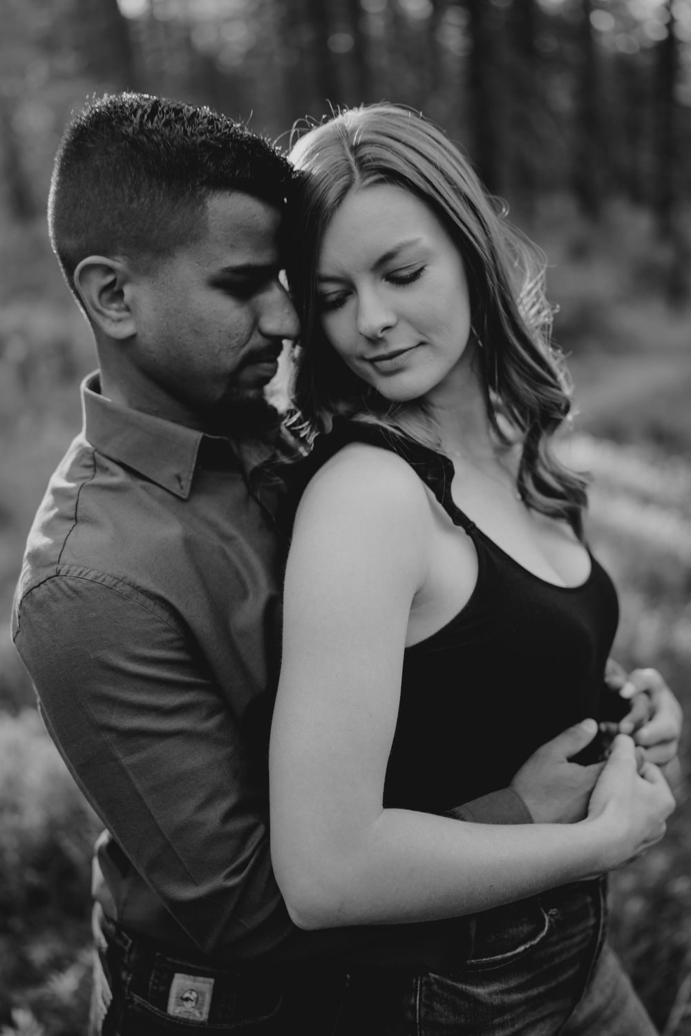 Black and white intimate portrait of couple embracing tenderly in forest during engagement shoot.