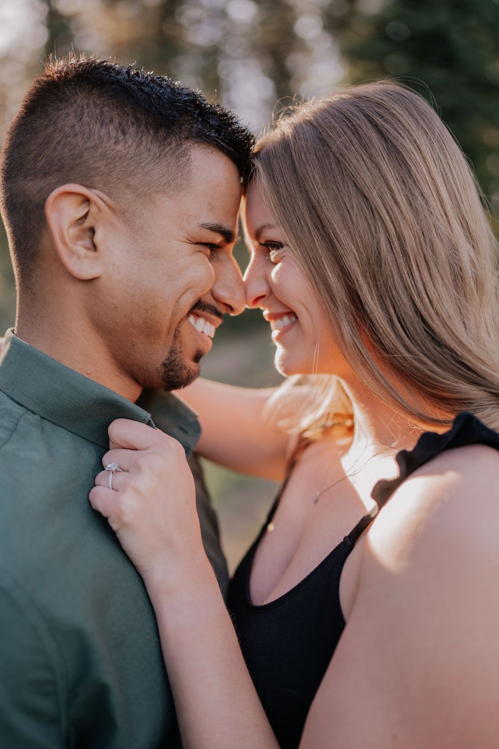Laughing couple touching foreheads and smiling in warm golden sunlight during engagement session.