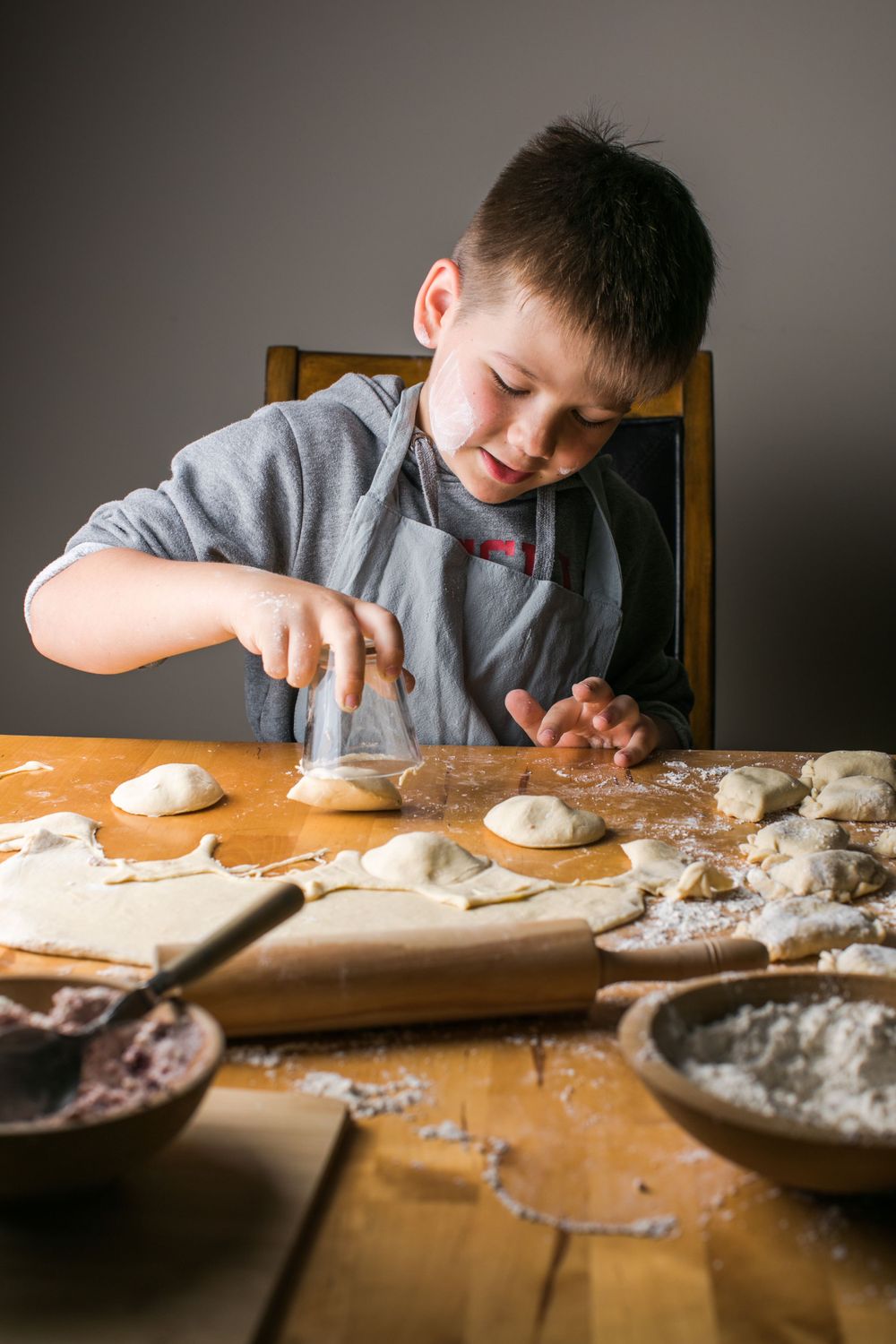 Child kneading and shaping dough on a wooden table while baking.