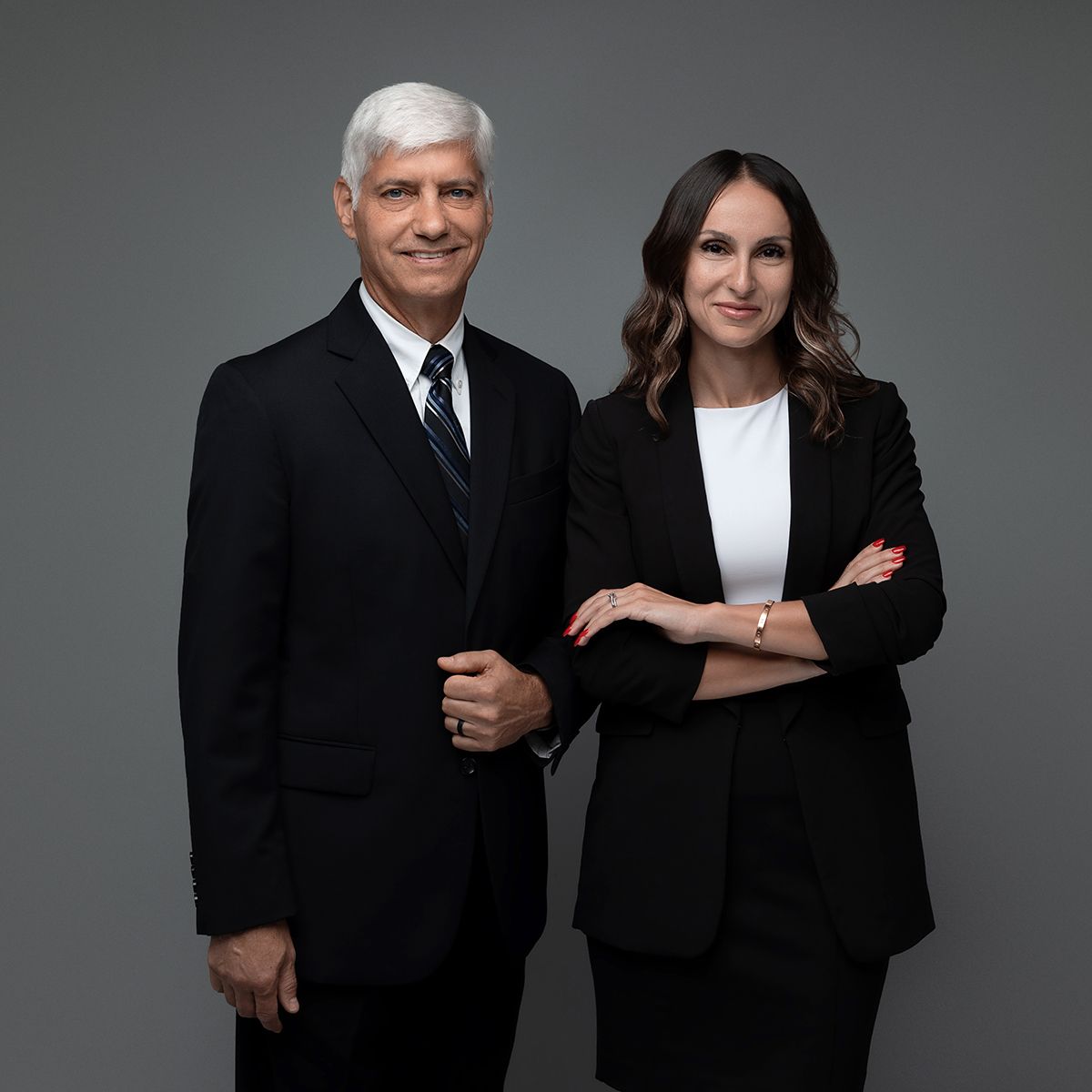 Professional business portrait of two colleagues in formal attire against grey background.