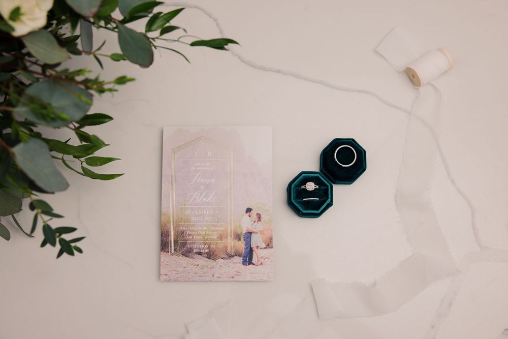 Wedding details flatlay with greenery, invitations and delicate accessories on white background.