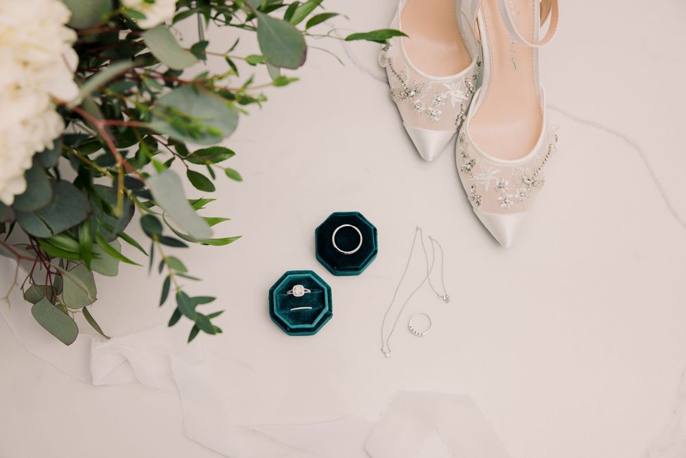Bridal shoes and floral details arranged with eucalyptus leaves on light background.