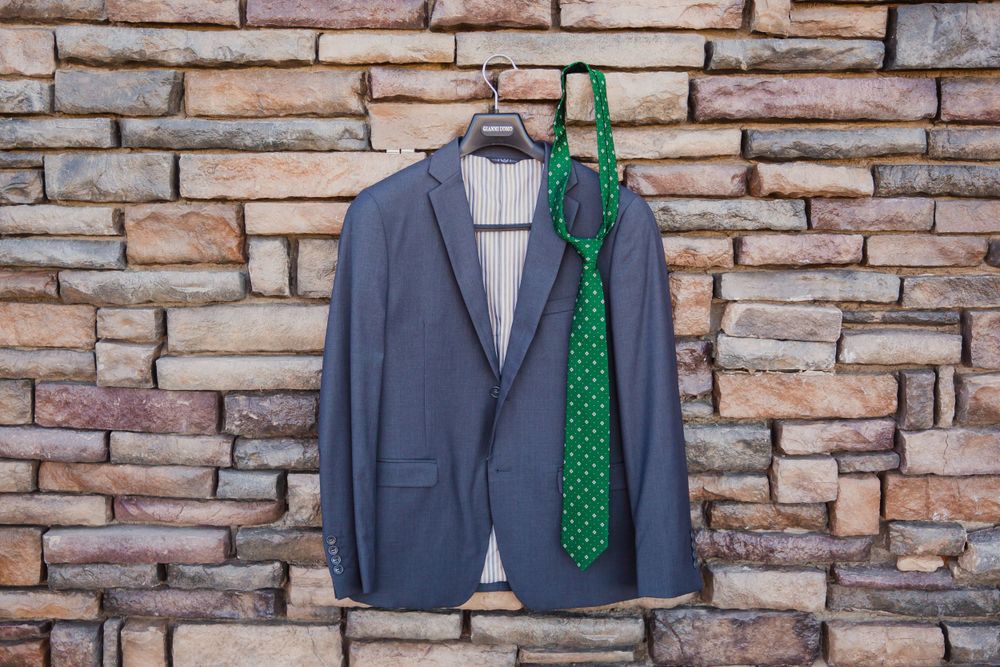 Row of grey groomsmen suits with emerald green polka dot ties against stone wall.