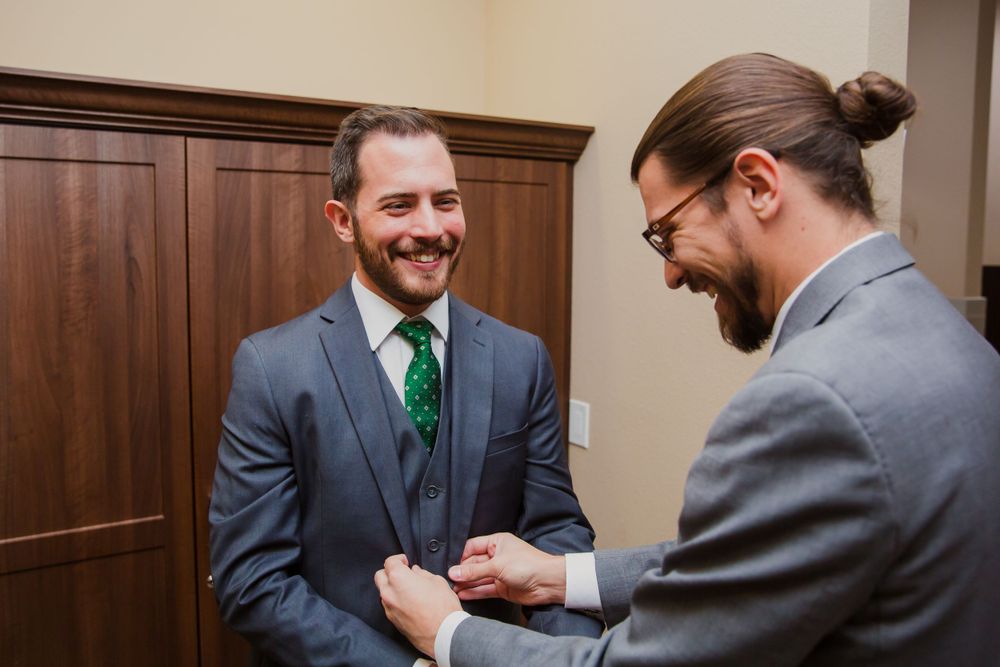 Groomsmen in grey suits and green ties prepare for wedding ceremony.