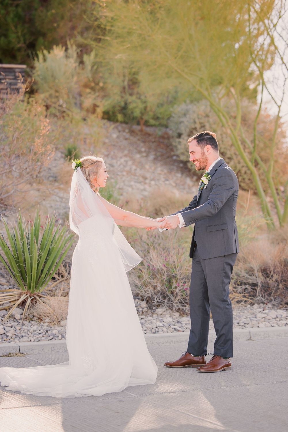 Bride and groom dancing together on a paved path surrounded by desert scenery.