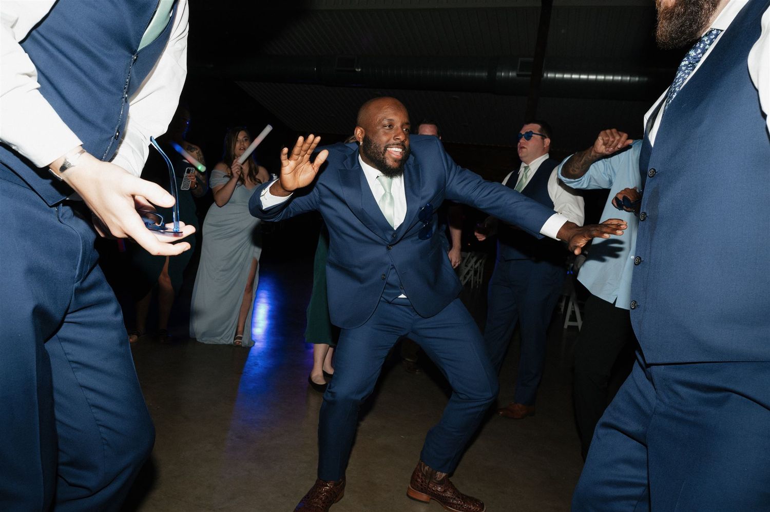 Wedding guest dancing enthusiastically in a navy suit surrounded by others on the dance floor.