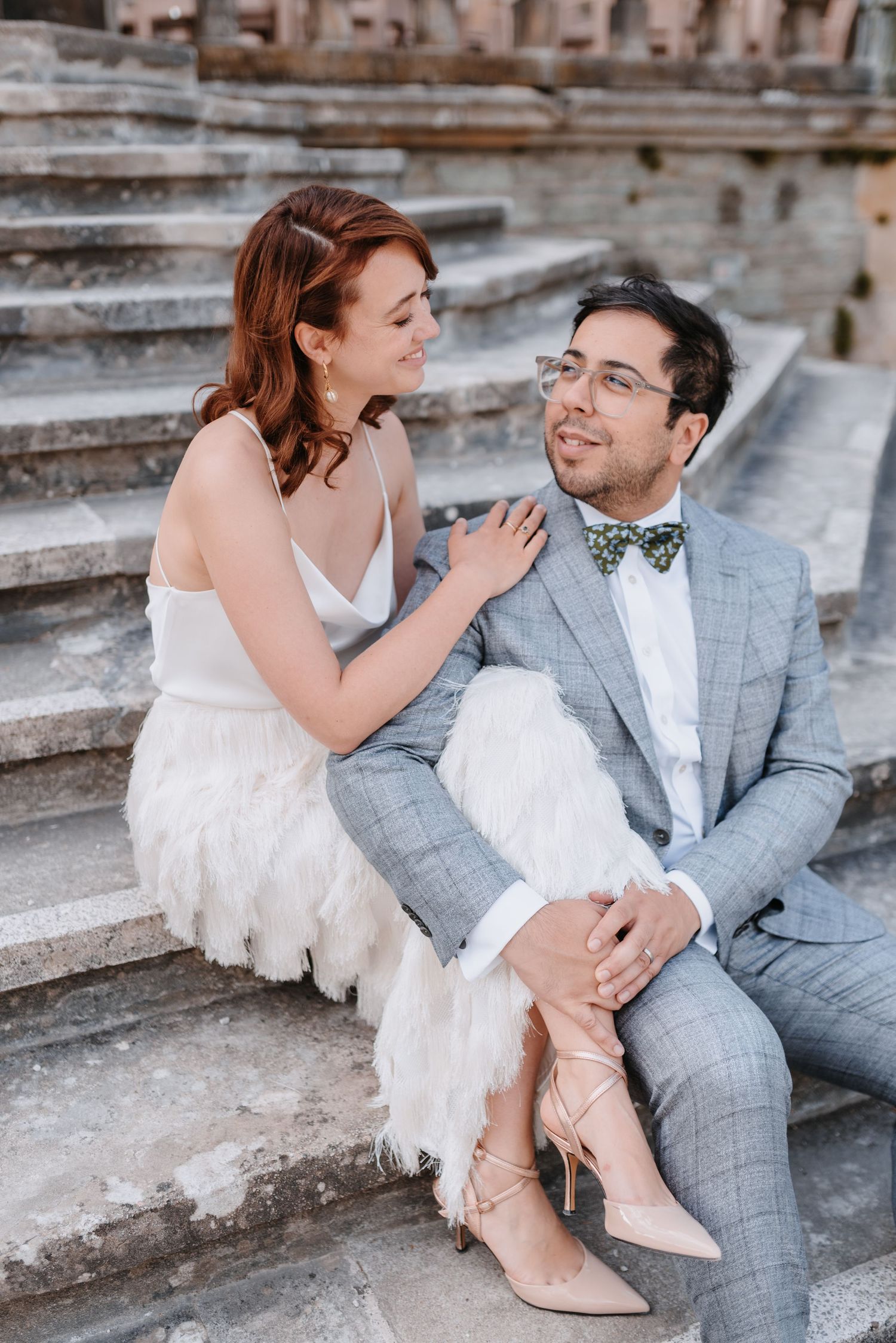 Couple in wedding attire sitting together on stone steps in romantic pose.