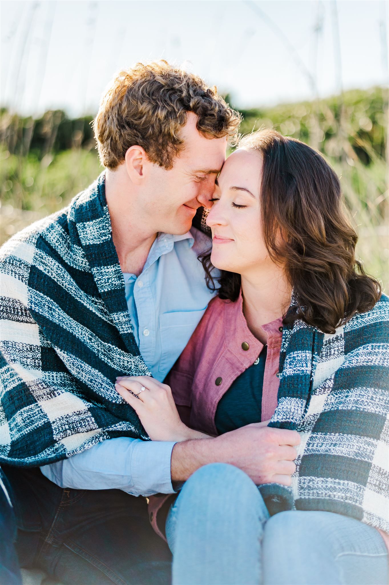 Romantic couple sharing intimate moment wrapped in blanket outdoors.