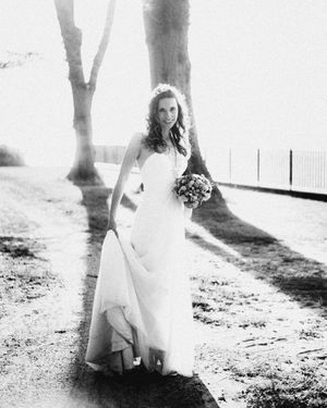 A bride in a flowing white dress holding a bouquet in a black and white outdoor portrait.
