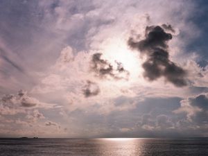 Dramatic sunset over ocean with dark clouds and reflective water.