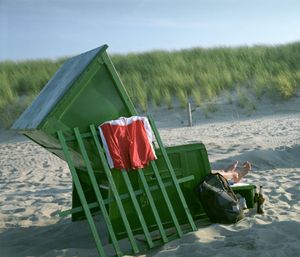 Green beach chair with red towel on sandy beach with tall grass.