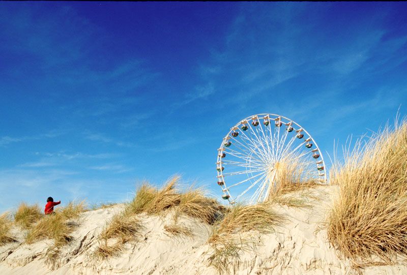 Ferris wheel rising above sand dunes against bright blue sky.