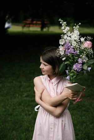 Woman in pink dress holding beautiful bouquet of lilacs and white flowers in garden setting.