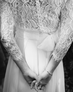 Close-up detail of delicate white lace sleeves and clasped hands in a wedding dress.
