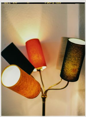Vintage floor lamp with multiple cylindrical shades in orange, brown and black creating warm ambient lighting.