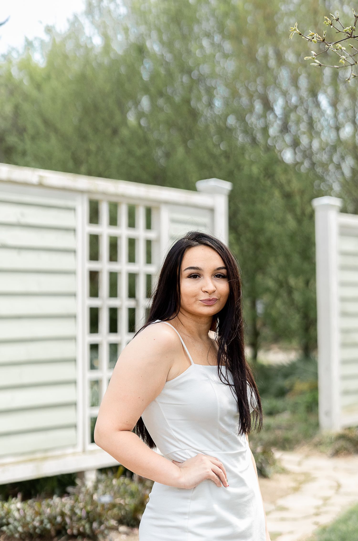 Elegant portrait against white lattice fence with trees in background.