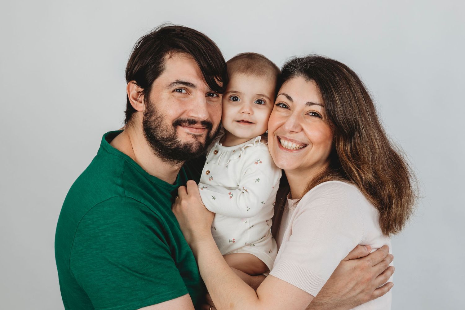 A studio portrait of a family of three sharing warm smiles together.